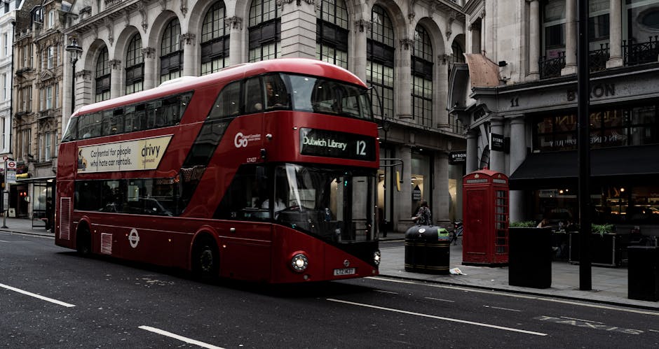 A red double-decker bus parked on a street in Dulwich Village, SE21, with its destination displayed as 'Dulwich Library' and route number 12. The bus is part of London’s public transport fleet, feat